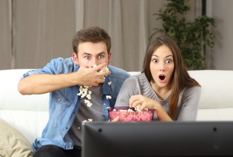 Amazed couple watching tv program sitting on a couch at home